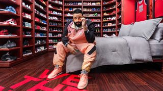 DJ Khaled seated in room filled with shelves of shoes.